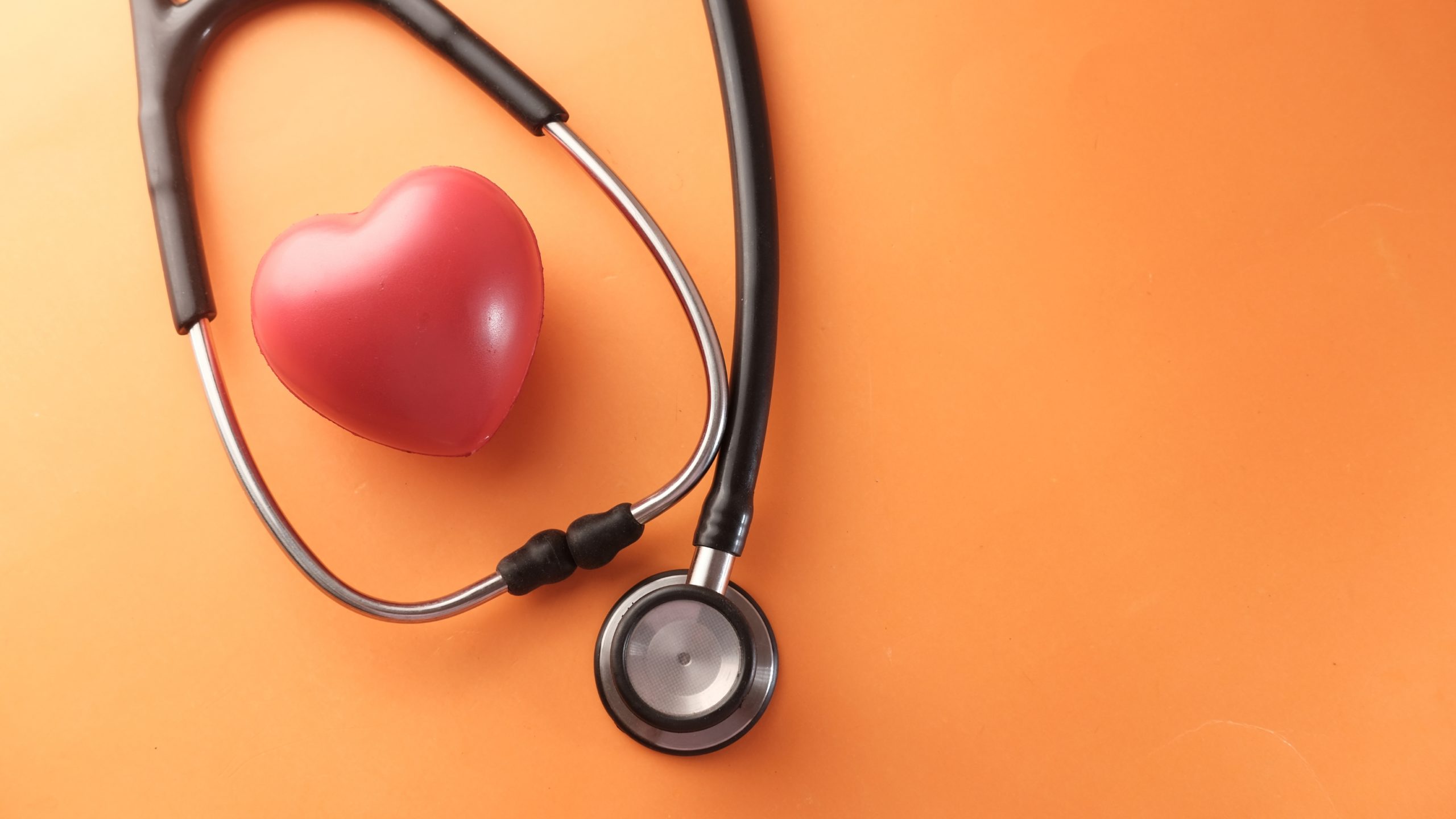 Estetoscopio y corazón rojo sobre fondo naranja, representando la importancia del diagnóstico genético preimplantacional en la reproducción asistida.