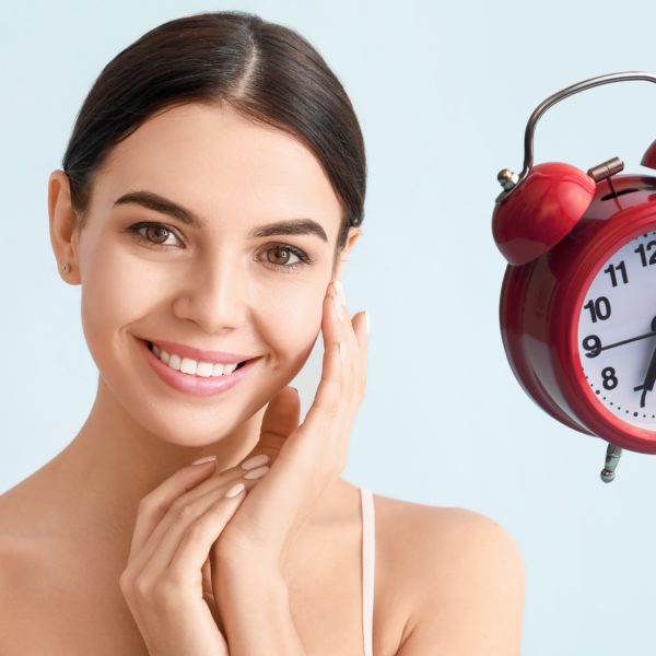 Mujer sonriente junto a un reloj despertador, simbolizando la importancia del tiempo en la vitrificación y congelación de gametos y embriones.